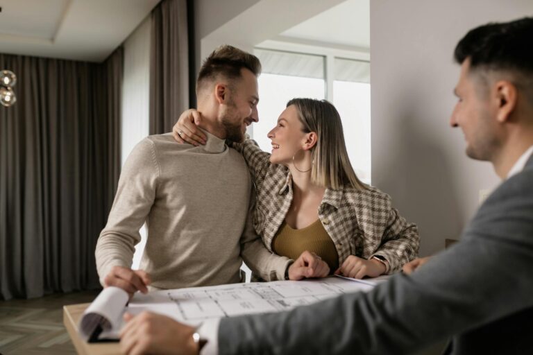 A cheerful couple discussing real estate plans with a realtor inside a modern home.